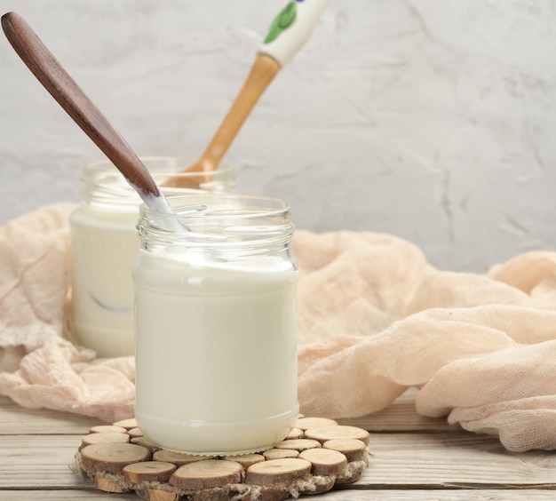 Homemade yogurt in a glass transparent jar on a wooden table, a healthy fermented milk product