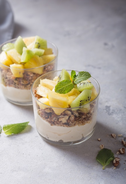 Homemade yogurt parfait with granola, kiwi fruit, pineapple and nuts in a glass for healthy breakfast on concrete background