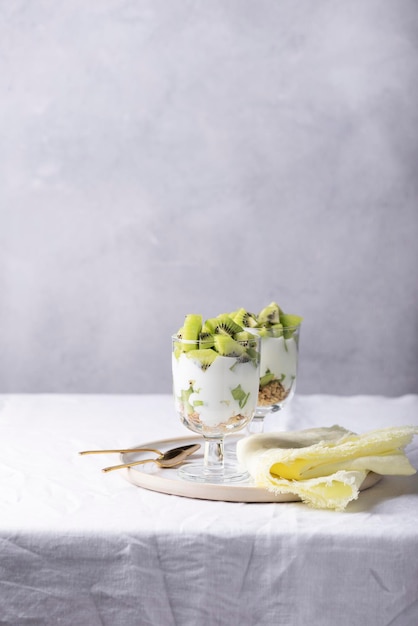 Homemade yogurt with fresh kiwi, muesli and mint on the white background, selective focus image