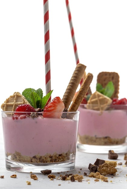 Домашний йогурт с красными ягодами, малиной, черникой, ежевикой и клубникой, печеньем и шоколадом на белом деревянном столе. Концепция здорового питания