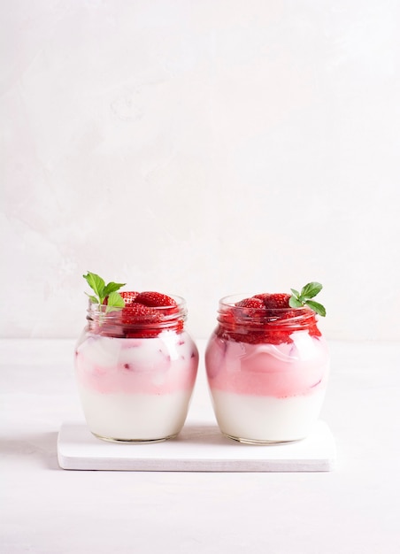 Homemade yogurt with ripe strawberries decorated with mint stands in banks on a wooden stand