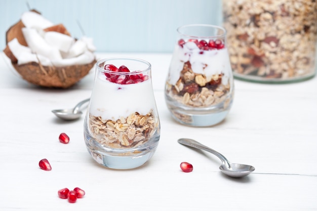 Yougurt fatto in casa con muesli e melograno in bicchieri sulla tavola di legno bianco. colazione salutare.