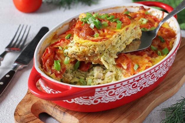 Photo homemade zucchini casserole with chicken tomatoes and cheese in a ceramic mold on wooden board closeup