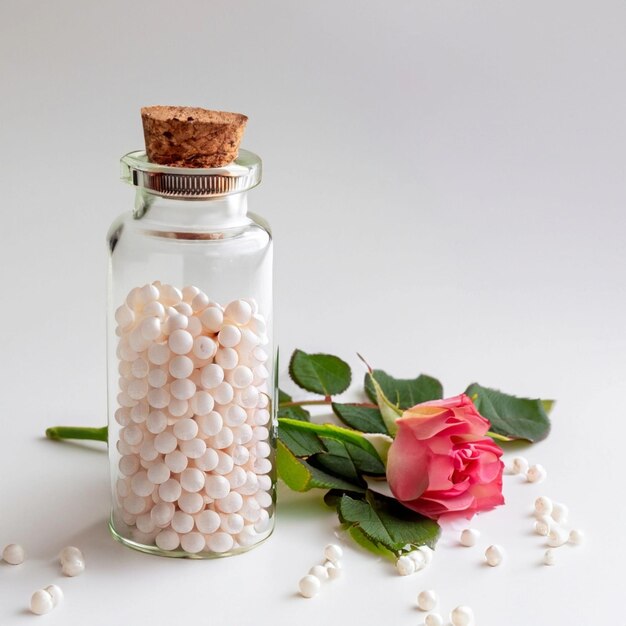 Гомеопатическая концепция Ромашка в прозрачной колбе и гомеопатические зерна на белом фоне