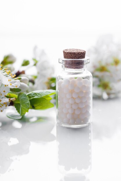 Homeopathic pills with spring flowers on white background