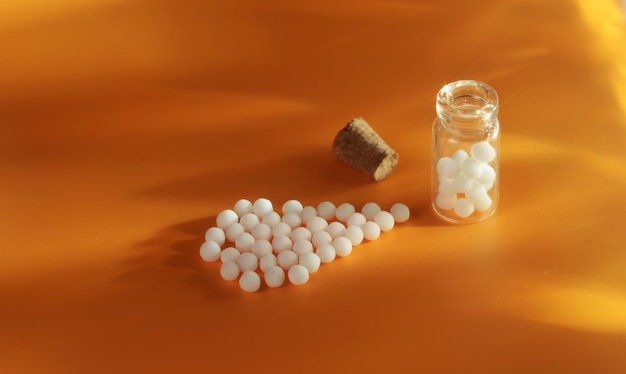 Homeopathische ballen in bulk en in een glazen pot op een oranje achtergrond, met de uitstraling van de zon