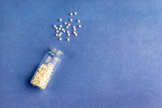 Homeopathische bolletjes (pillen) en glazen fles op blauwe achtergrond. Het concept van gezondheidszorg en alternatieve kruidengeneeskunde: homeopathie en natuurgeneeskunde. Flatlay, bovenaanzicht,