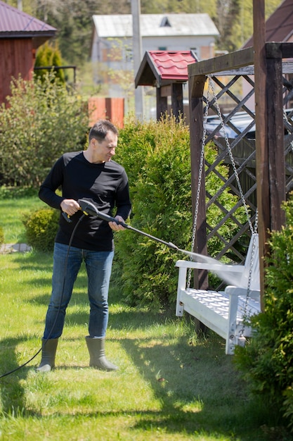 Photo homeowner washes white wooden swing with high pressure washer