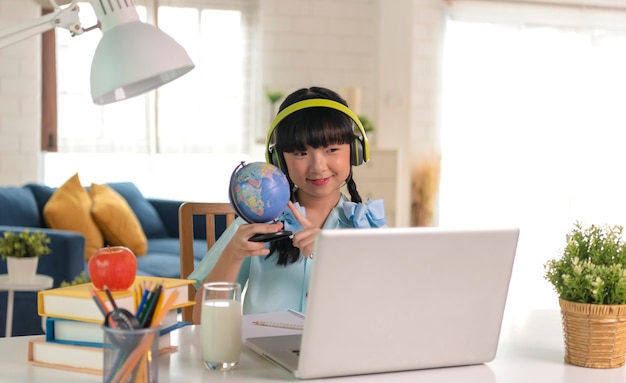 Homeschool Asian little young girl student learning virtual internet online class on table at home.