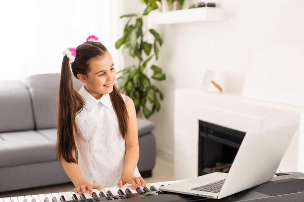 Homeschool little young kid girl learning piano from computer connecting to internet music online class by school teacher. New normal lifestyle and education, student study at home concept.