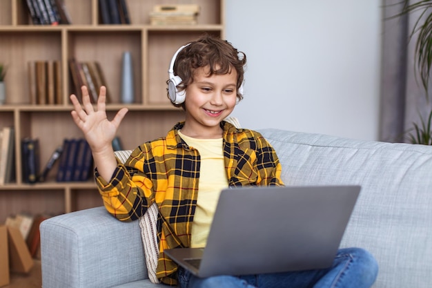 Homeschooling concept Cute little boy wearing headset video chatting with teacher via laptop waving hand and smiling