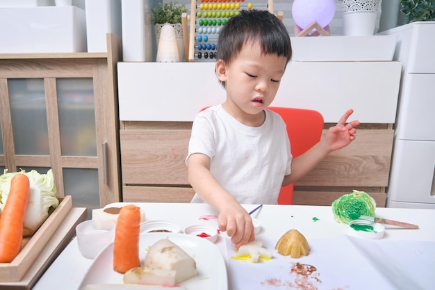 ホームスクーリングかわいいアジアの幼稚園の男の子の子供が家で野菜のスタンプからアートワークを作る幼児や小さな子供のための楽しいアートや工芸品子供向けアートプロジェクト