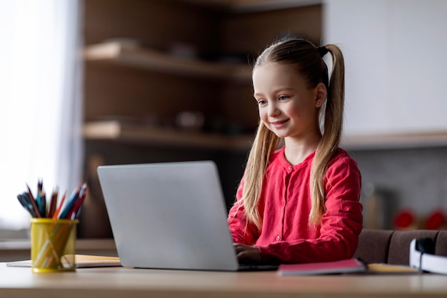 Foto studio della ragazza del preteen homeschooling sul computer portatile a casa utilizzando la piattaforma educativa