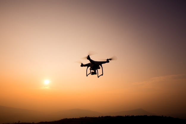 Foto hommelsilhouet die in zonsonderganglandschap vliegen met digitale camera bij zonsondergang klaar te vliegen.