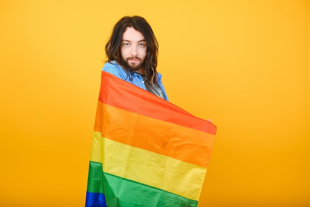 Homo man met een gay pride-vlag glimlachend en wegkijkend op gele achtergrond