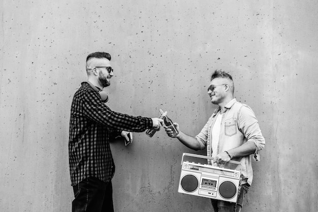 Homo paar bier drinken buiten terwijl u naar muziek luistert met een vintage boombox-tapespeler Hipster volwassen jongens die hun vriendschap vieren tijdens het weekend Zwart-wit stijl