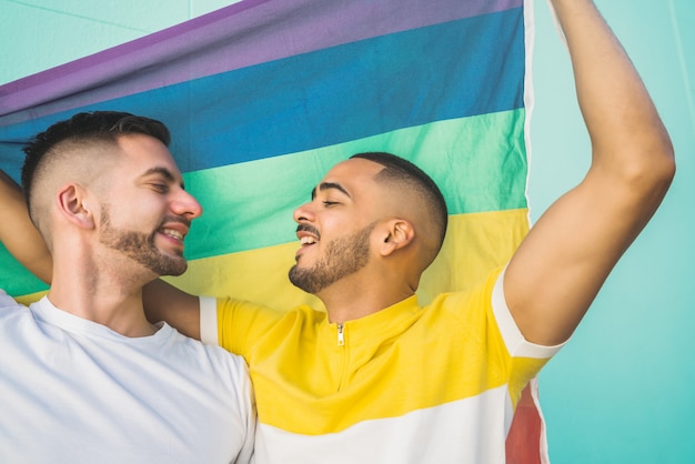 Foto homopaar die en hun liefde met regenboogvlag omhelzen tonen.