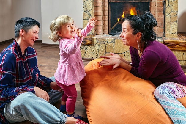 Homoseksueel stel speelt met hun stiefdochter, ze zitten op zitzakken en glimlachen terwijl ze naar het kleine meisje kijken.