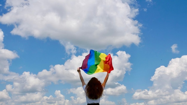 Homoseksuele lesbische vrouw met een regenboog Lgbt-genderidentiteitsvlag op de hemelachtergrond met wolken op een zonnige dag en een homoparade vieren Biseksualiteit Day of National Coming Out Day