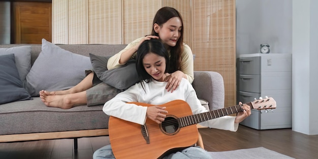 Homoseksuele LGBT-jonge vrouwen die gitaar spelen en zingen in de woonkamer met geluksmoment