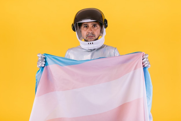 Homoseksuele man verkleed als astronaut met een helm en zilveren pak met de vlag van het trans-collectief op een gele achtergrond Homo-homoseksuele transrechten en gender pride-concept