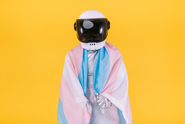 Homoseksuele man verkleed als astronaut met een helm en zilveren pak met een vlag van de trans-gemeenschap op een gele achtergrond Homo-homoseksuele transrechten en gender pride-concept