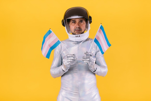 Homoseksuele man verkleed als astronaut met een helm en zilveren pak met kleine trans-vlaggen op een gele achtergrond Homo-homoseksuele transrechten en gender pride-concept