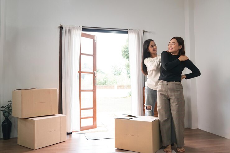 Photo 同性愛者の幸せな若いアジア人女性は、新しい賃貸住宅に引っ越しながら持ち物を運びながら体の痛みのガールフレンドをマッサージするのを手伝います