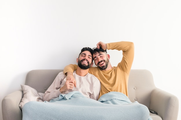 Homosexual young gay couple enjoying together on sofa against white wall