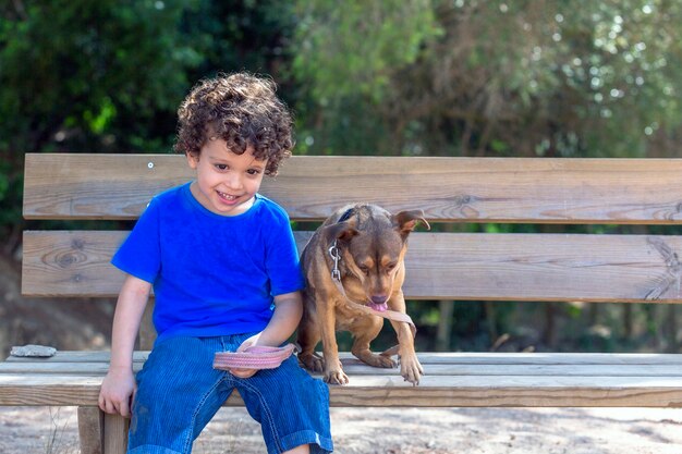 hond en kind zittend op een houten bankje in het park naar beneden kijkend rustend na het spelen