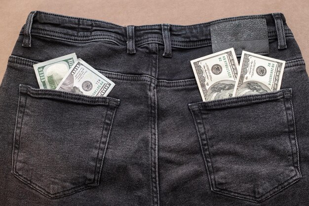 Honderd-dollarbiljet steekt uit de zak van een zwarte spijkerbroek