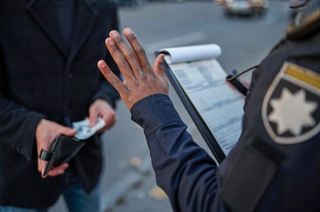 An honest police officer refuses to take a bribe from male driver. Policeman in uniform protect the law, registration of an offense. Cop works on city street, order and justice control