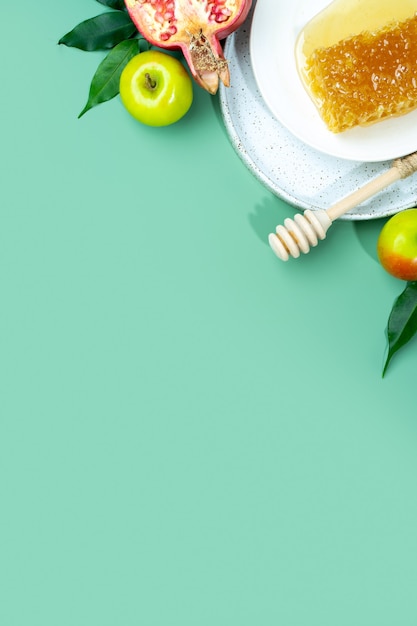 Foto miele, mela e melograno su fondo verde menta. concetto capodanno ebraico felice vacanza rosh hashanah. layout creativo di simboli tradizionali. vista dall'alto. disposizione piatta. copia spazio. shana tova.