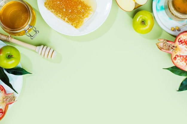 Honey, apple and pomegranate on a mint-green background. Concept Jewish New Year Happy holiday Rosh Hashanah. Creative layout of traditional symbols. View from above. Flat lay. Copy space. Shana Tova.