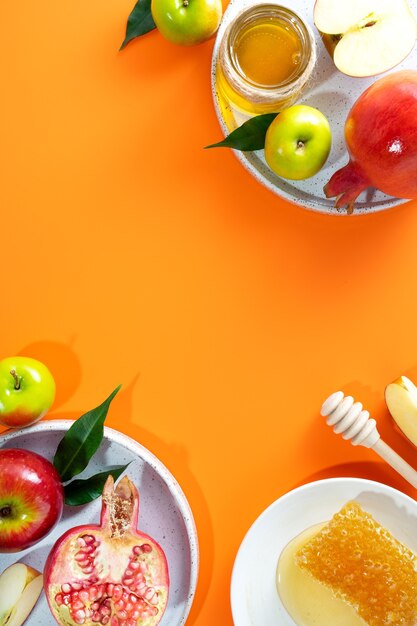 Honey, apple and pomegranate on a orange background. Concept Jewish New Year Happy holiday Rosh Hashanah. Creative layout of traditional symbols. View from above. Flat lay. Copy space. Shana Tova.