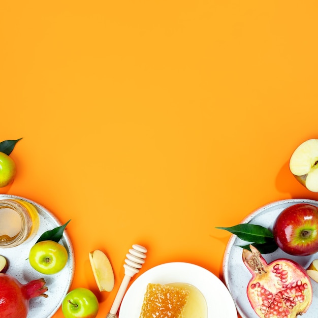 Honey, apple and pomegranate on a orange background. Concept Jewish New Year Happy holiday Rosh Hashanah. Creative layout of traditional symbols. View from above. Flat lay. Copy space. Shana Tova.