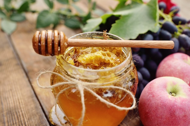 Honey in a beautiful jar, wooden spoon spindle, grapes and apples on a wooden background