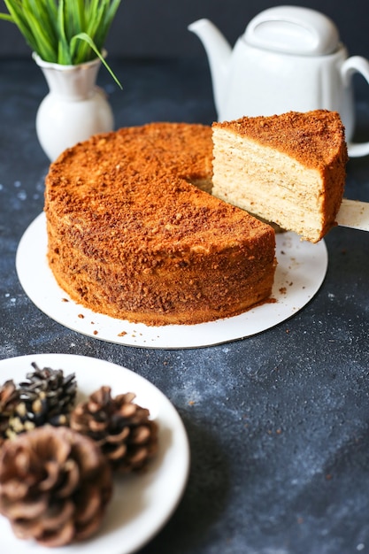 honey cake on dark table with flowers, teapot and cones