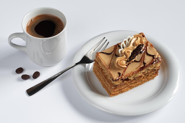 Honey cake with cream and cup of hot coffee on white background