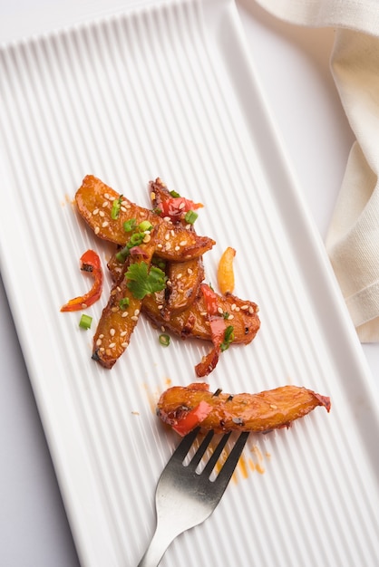 Honey Chilli Potato Wedges, popular Indian-Chinese starter recipe, garnished with sesame and onion. selective focus