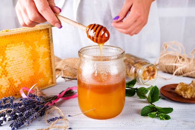 Honey combs and a jar with fresh honey mint leaves and lavender on a white wooden table. 