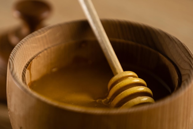 Honey dripping from honey dipper in wooden bowl. Close-up. Healthy organic. Thick honey dipping from the wooden honey spoon, closeup