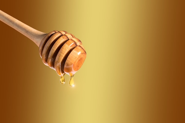 Honey dripping from honey dipper on yellow surface.