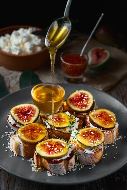 Honey dripping from a spoon onto fig sandwiches on toasted goat cheese baguette on a plate