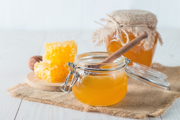 Honey dripping from a wooden honey dipper in a jar on wooden grey rustic