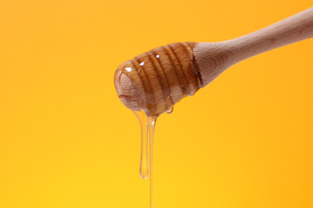 Мед капает из деревянной ложки для меда на цветном ярком фоне