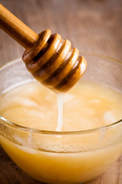 Honey dripping in glass bowl on wooden table