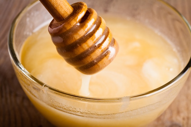 Honey dripping in glass bowl on wooden table