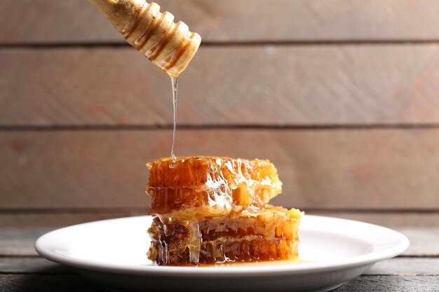 Honey dripping on honeycombs on plate on wooden background