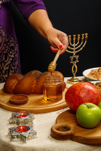 Honey drips from a wooden spoon in a woman's hand next to the menorah challah and couscous and pomegranate